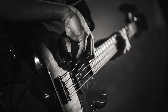 Black and white close up of man playing base guitar